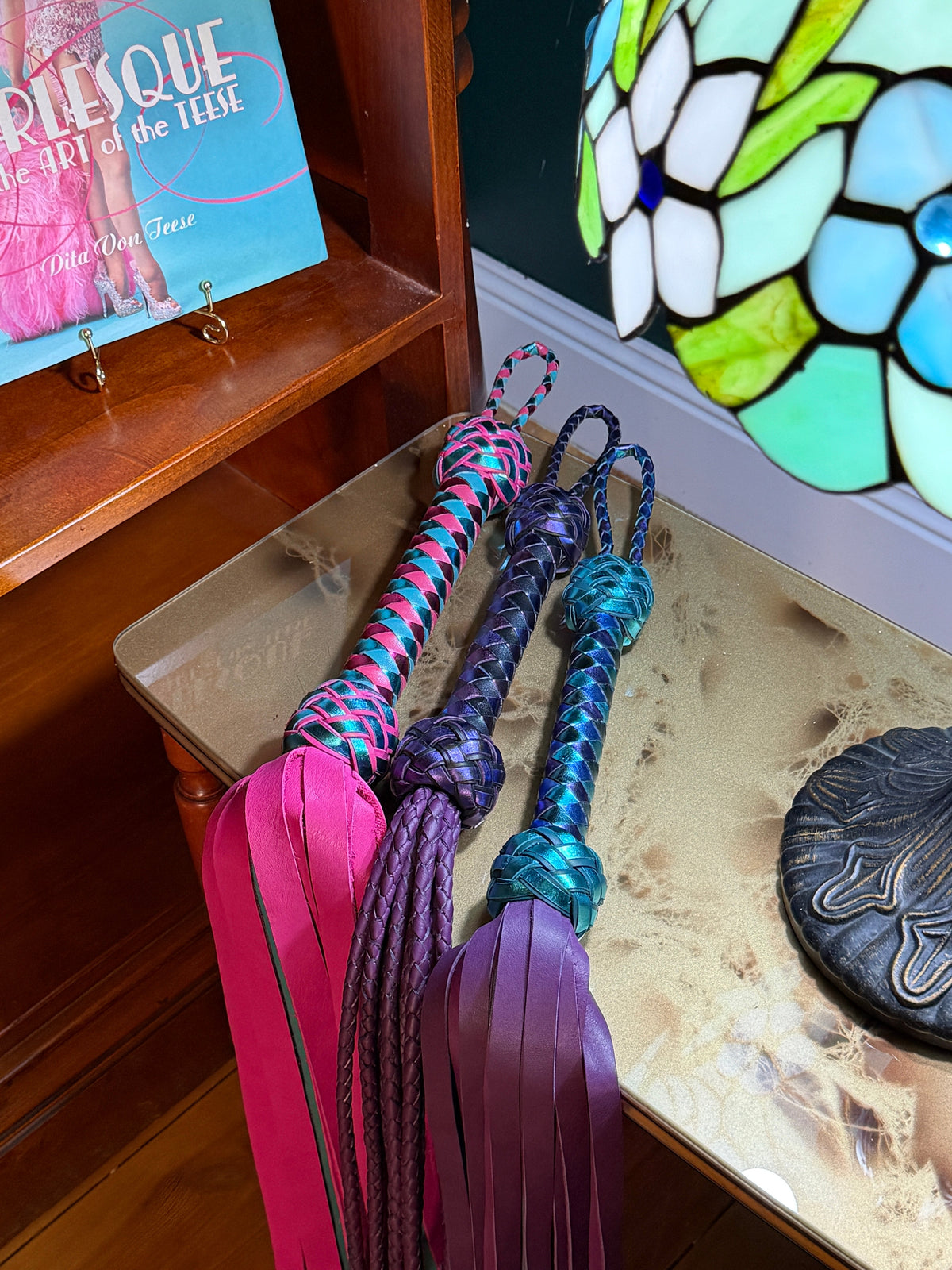 Jewel-toned leather floggers under a Tiffany lamp against a green wall, The Menagerie by Collared Foxy