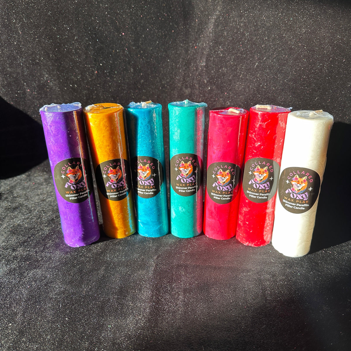 Row of shimmer and metallic paraffin wax play candles on black velvet, Collared Foxy