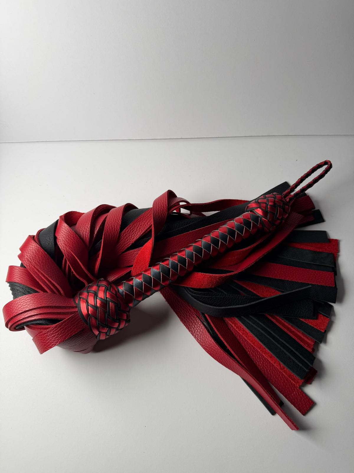 Garnet flogger, red and black floater cowhide falls with a metallic red and black box braid handle
