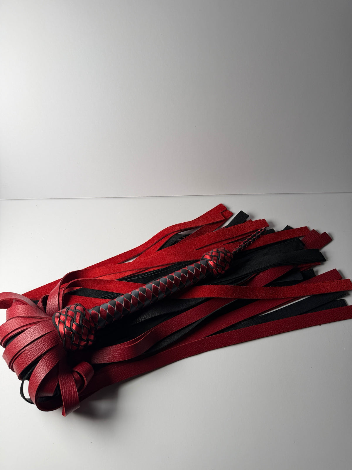 Garnet flogger laid out, long red and black floater falls beneath a metallic red and black handle