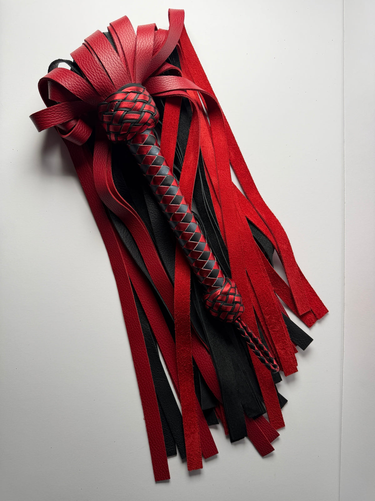 Garnet flogger from above, red and black floater cowhide falls fanned around the braided handle