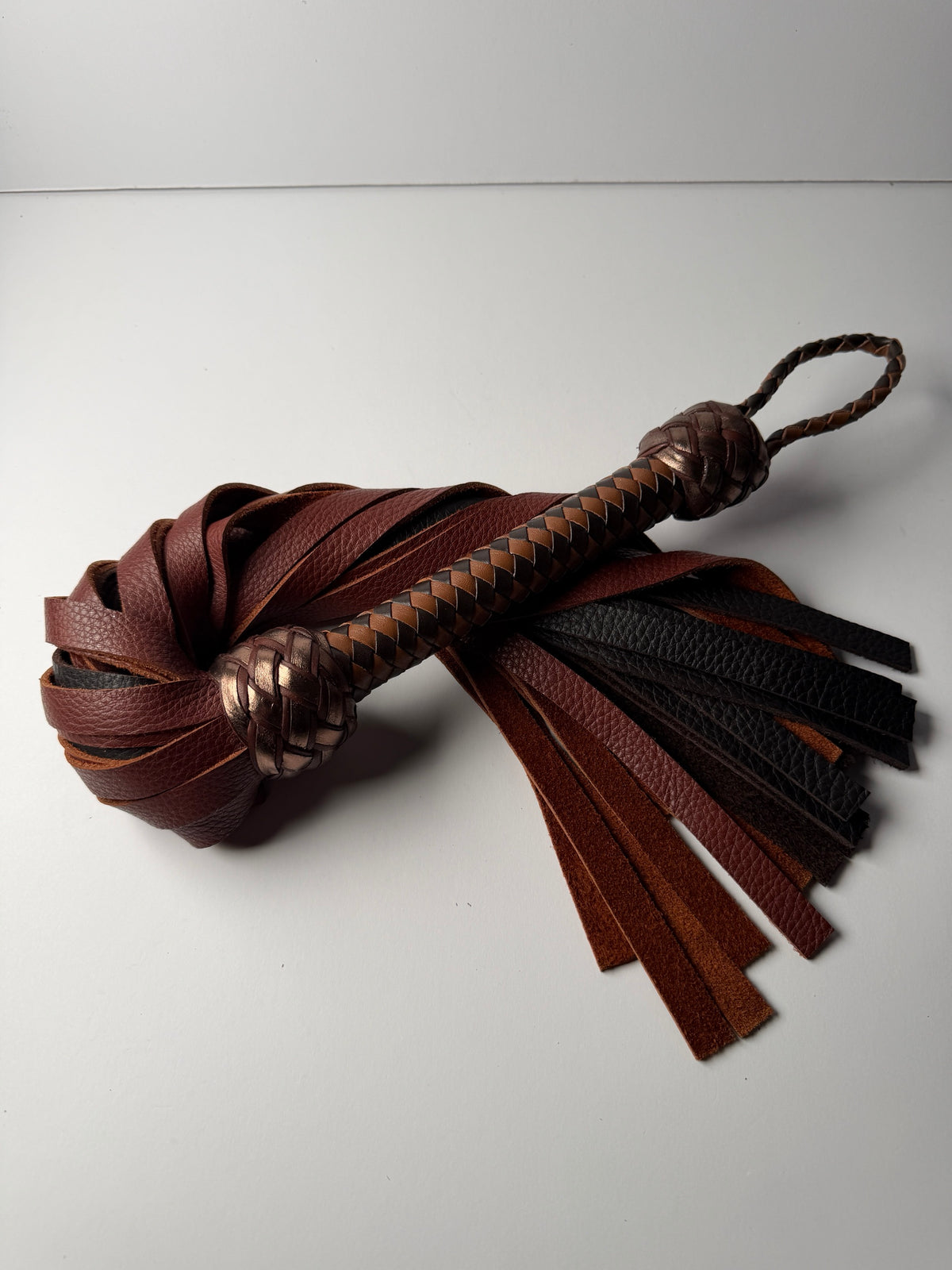 Oloroso flogger, whisky and chocolate floater cowhide falls with a chocolate and tan braided handle and metallic bronze Turk's head knots