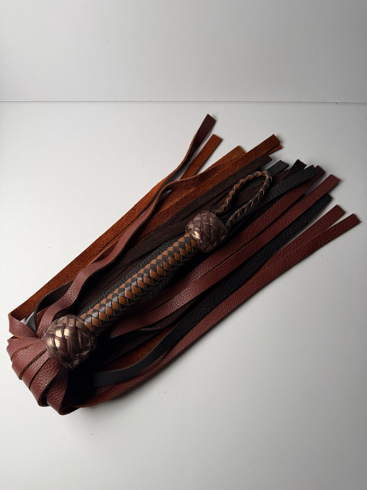 Oloroso flogger laid flat, whisky and chocolate floater cowhide falls spread beneath the braided handle