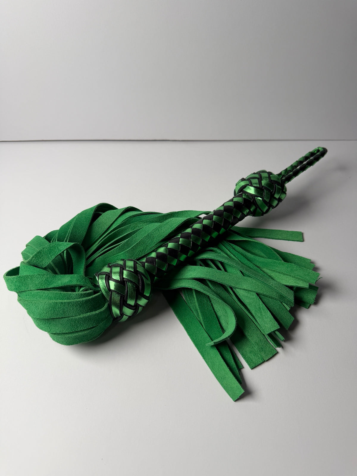 Peridot flogger, green cowhide suede falls with a metallic green and black braided handle and Turk's head knots