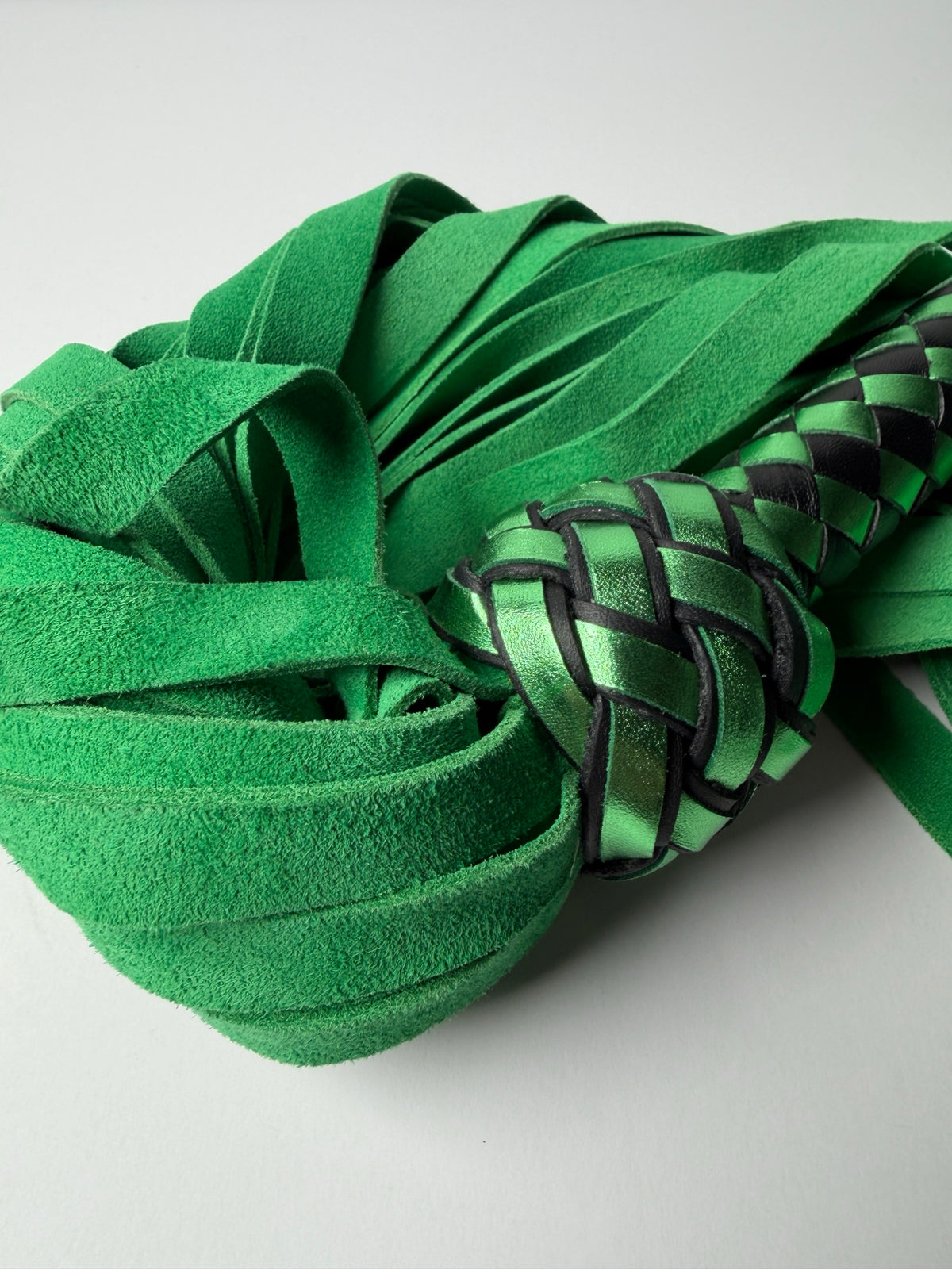 Close up of Peridot's green cowhide suede falls curled around a metallic green and black Turk's head knot