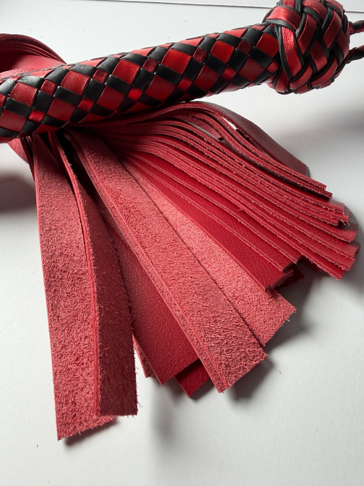Red cowhide fall tips on the Vermilion flogger, showing grain and suede side